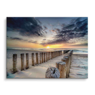 Holzsteg am Sandstrand im Sonnenuntergang mit dramatischem Himmel über dem Meer