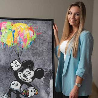 Frau präsentiert modernes Wandbild mit Comic-Maus und bunten Luftballons auf grauem Hintergrund