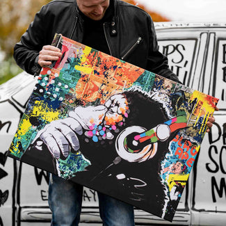 Buntes Pop Art Wandbild mit Affe und Kopfhörern, gehalten von Mann vor Graffiti-Auto
