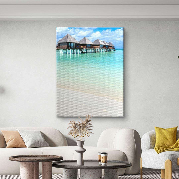 Modernes Wohnzimmer mit Leinwandbild von Überwasser-Bungalows am türkisfarbenen Meer an der Wand.