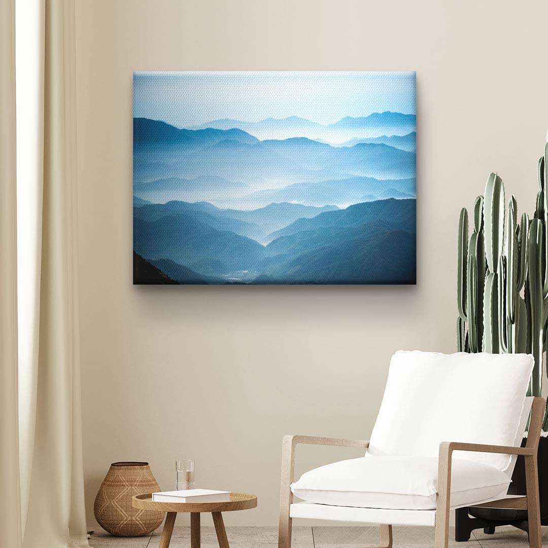 Modernes Wandbild auf Leinwand mit abstrakten blauen Bergen im Wohnzimmer mit Kaktus und Sessel