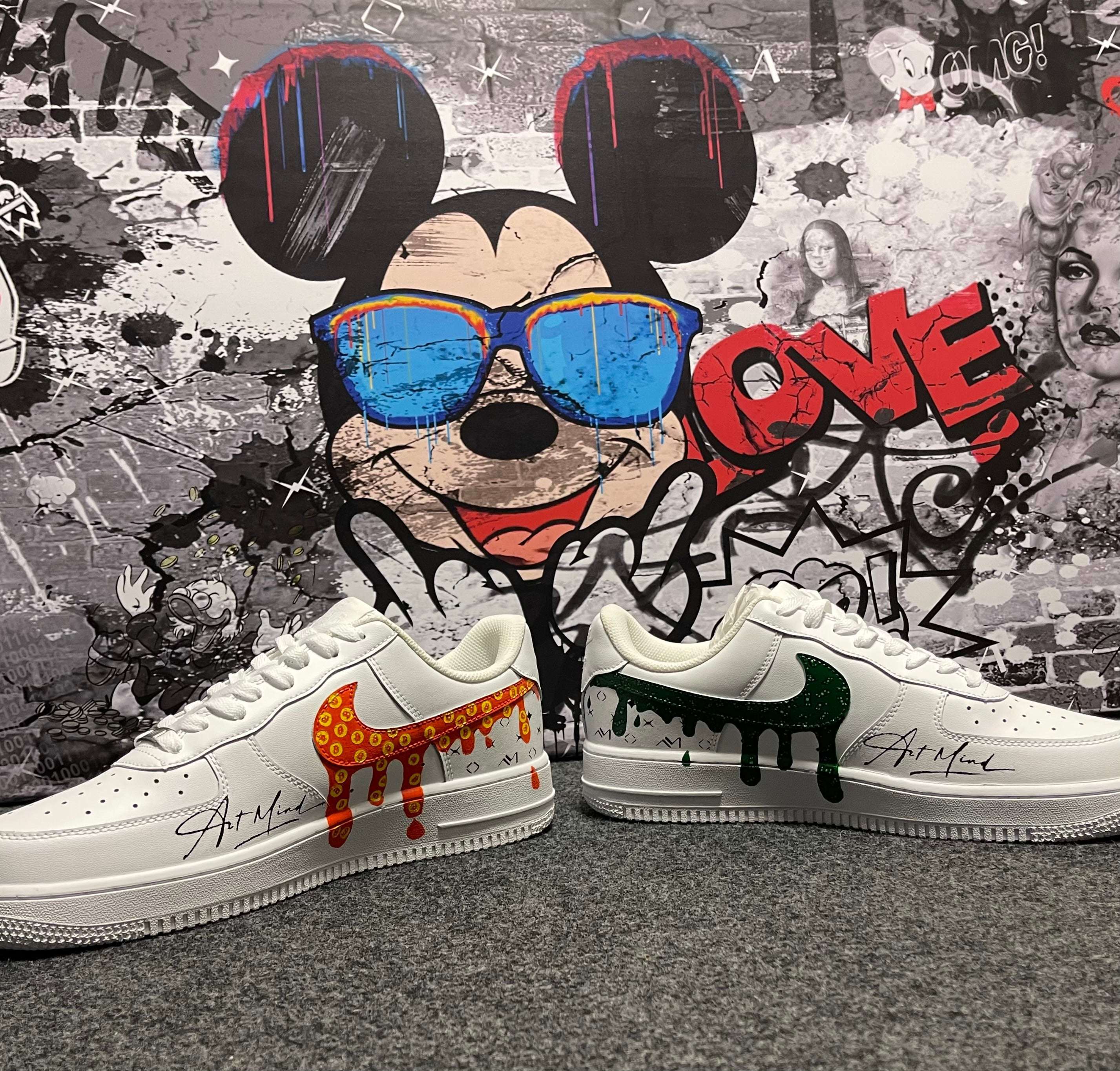 Weißes Sneaker-Paar mit buntem, tropfendem Swoosh vor urbanem Wandbild mit Comic-Motiv.
