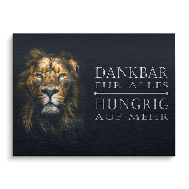 Motivationsbild mit Löwenportrait und dem Spruch 'Dankbar für alles, hungrig auf mehr' auf dunklem Hintergrund