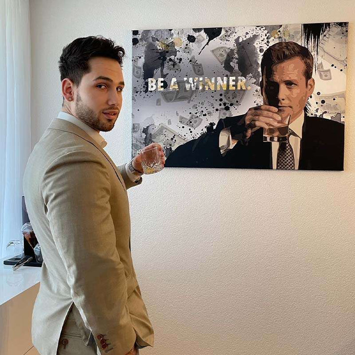 Mann im Anzug mit Glas vor Motivationsbild mit Schriftzug 'Be a winner' an Wand