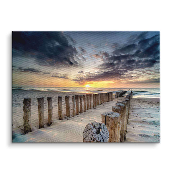 Holzsteg am Sandstrand im Sonnenuntergang mit dramatischem Himmel über dem Meer