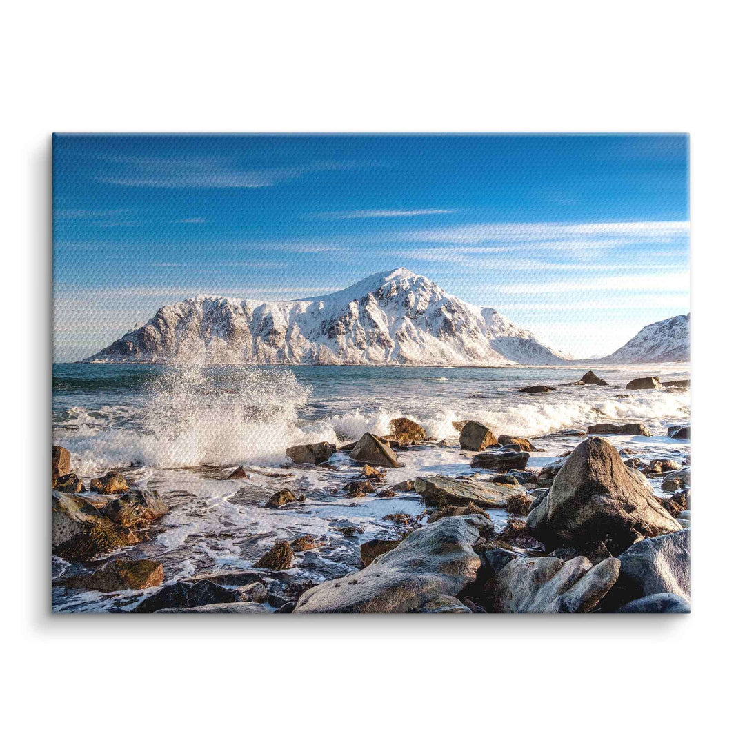 Wandbild mit verschneitem Berg, stürmischer Meeresküste und Felsen unter blauem Himmel