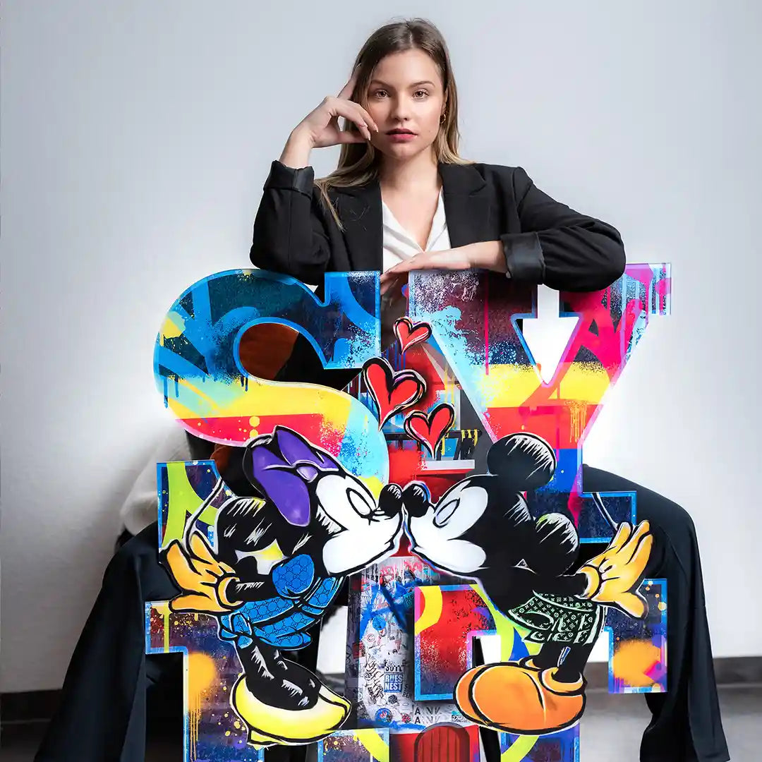 Buntes Wandbild im Comic-Stil mit küssenden Mäusen vor großer Buchstaben-Skulptur, Frau im Hintergrund