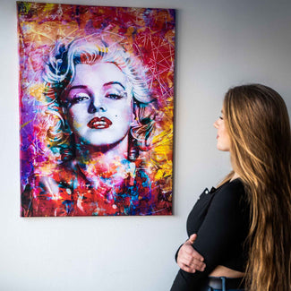 Frau betrachtet buntes Pop Art Wandbild einer berühmten Frau mit leuchtenden Farben an der Wand.