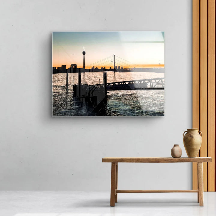 Modernes Wandbild mit Fluss, Brücke und Skyline bei Sonnenuntergang im Wohnzimmer